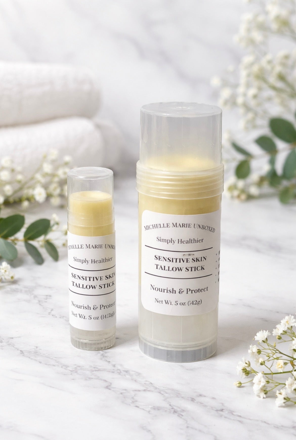 Two tallow sticks Sensitive Skin on a marble surface with flowers in the background